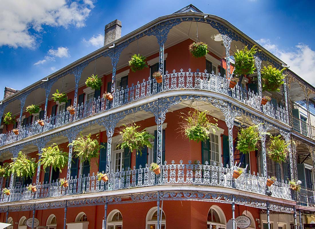 Covington, LA - View of an Old Three Story Building with Wrap Around Balconies with Hanging Plants in Covington Louisiana Against a Cloudy Blue Sky