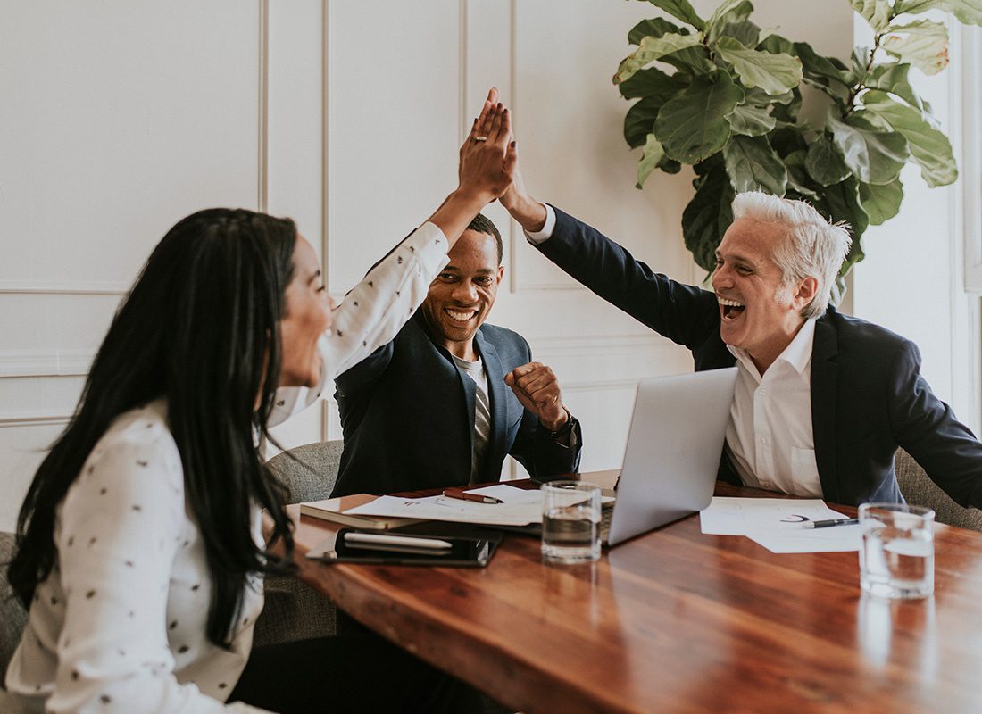 Risk Management - Portrait of a Group of Smiling Business Professionals Giving Each Other High Five During a Meeting in a Modern Office