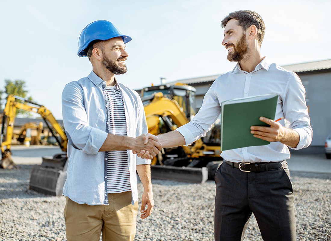 Surety Bond - Portrait of a Businessman Shaking Hands with a Cheerful Young Contractor as They Both Stand on a Construction Jobsite with Heavy Equipment in the Background
